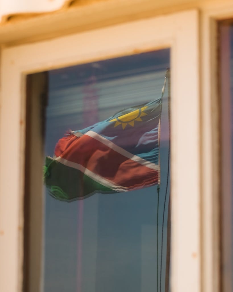 Namibian flag reflected in a window against an urban backdrop, showcasing national pride.
